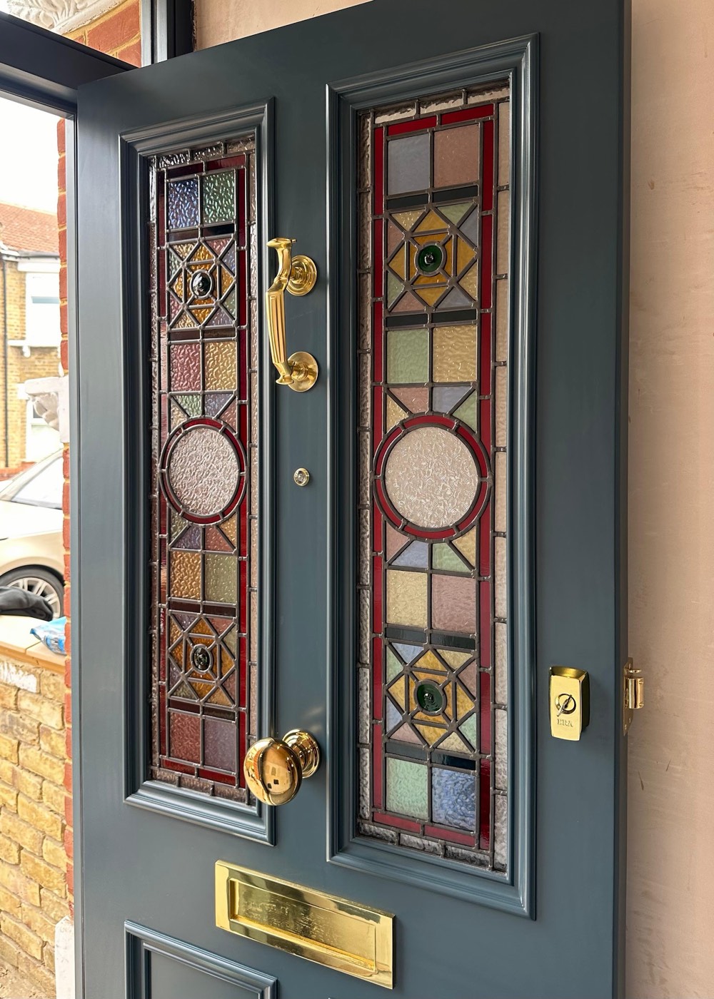 A bespoke heritage-green timber front door made by Beechhall Joinery, with two tall stained and leaded glass panels and polished brass door furniture.