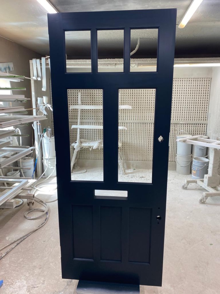 A navy-blue glazed front door with brass knob, freshly sprayed and drying in Beechhall Joinery's finishing booth.
